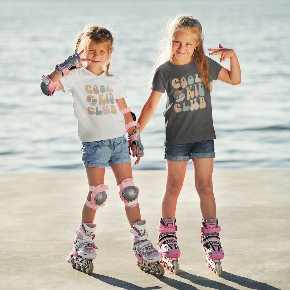 sisters wearing matching slowpoke maniac brand 'cool kid club' shirts, posing with peace signs and rollerblading by the beach